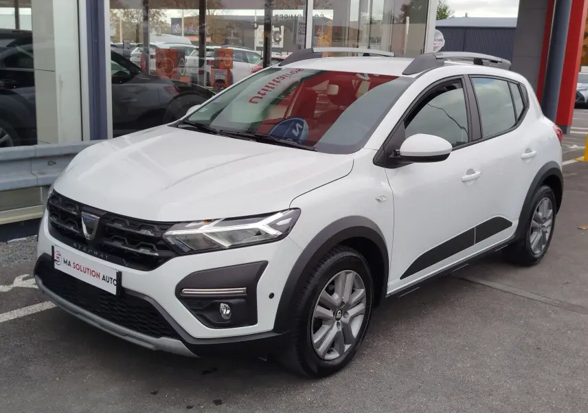 Vue 3/4 avant droite d'une Dacia Sandero Stepway blanche Glacier avec barres de toit et protections noires sur les ailes.