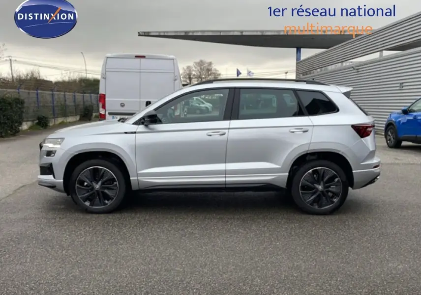 Vue de profil côté gauche d'un Skoda Karoq gris argent métal 2025 avec jantes noires et toit blanc.