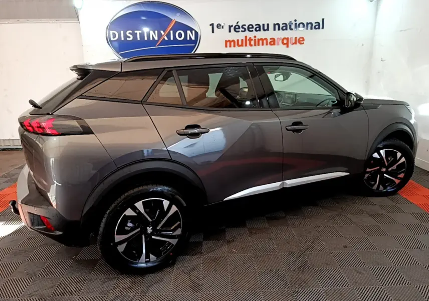 Vue côté droit d’un Peugeot 2008 gris foncé 2022 avec jantes noires et toit noir dans un showroom.