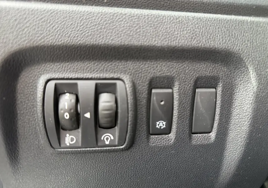 Gros plan sur les commandes de réglage des phares et du tableau de bord du Renault Captur blanc 2017, version Intens.
