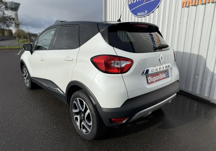 Renault Captur blanc 3/4 arrière droit avec toit noir et jantes alliage, stationné devant un bâtiment commercial.