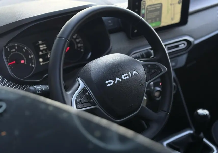 Vue intérieure centrée sur le volant noir DACIA avec tableau de bord et écran tactile GPS en arrière-plan.