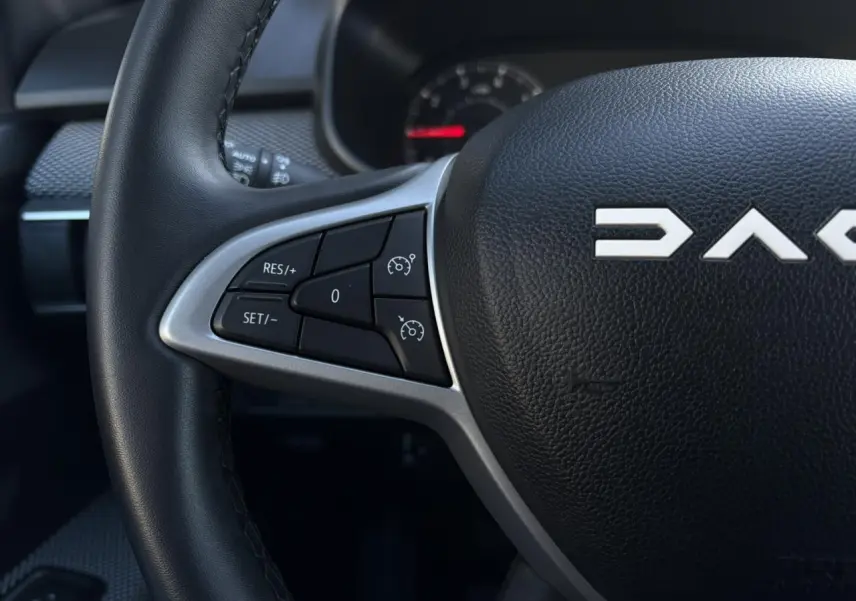 Gros plan sur le volant noir de la Dacia Jogger 2025 avec commandes de régulateur de vitesse et logo central partiel.