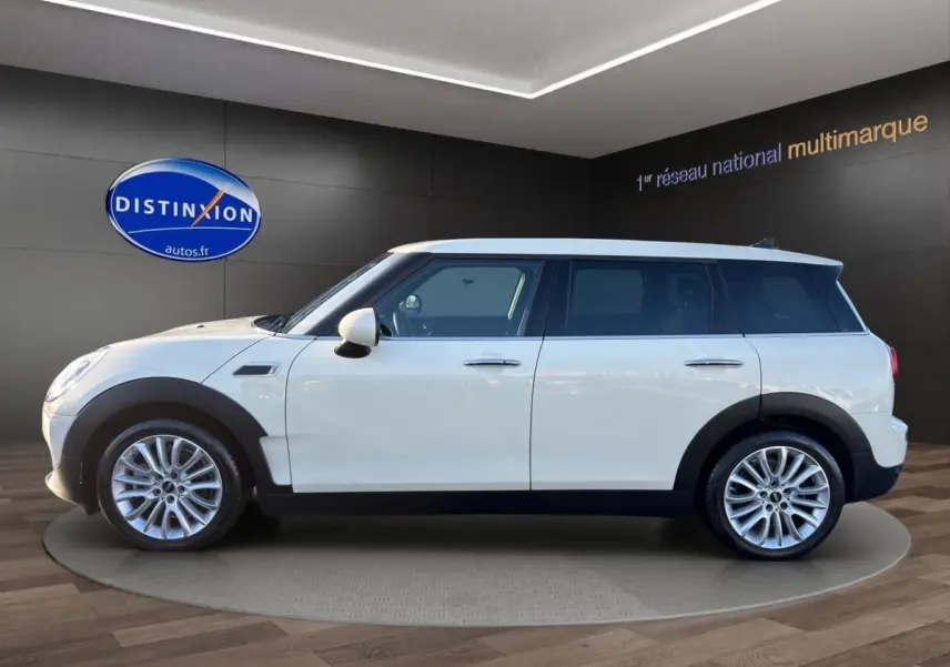 Vue de profil côté gauche d'une MINI Clubman Cooper Exquisite blanche avec jantes alliage et protections noires.