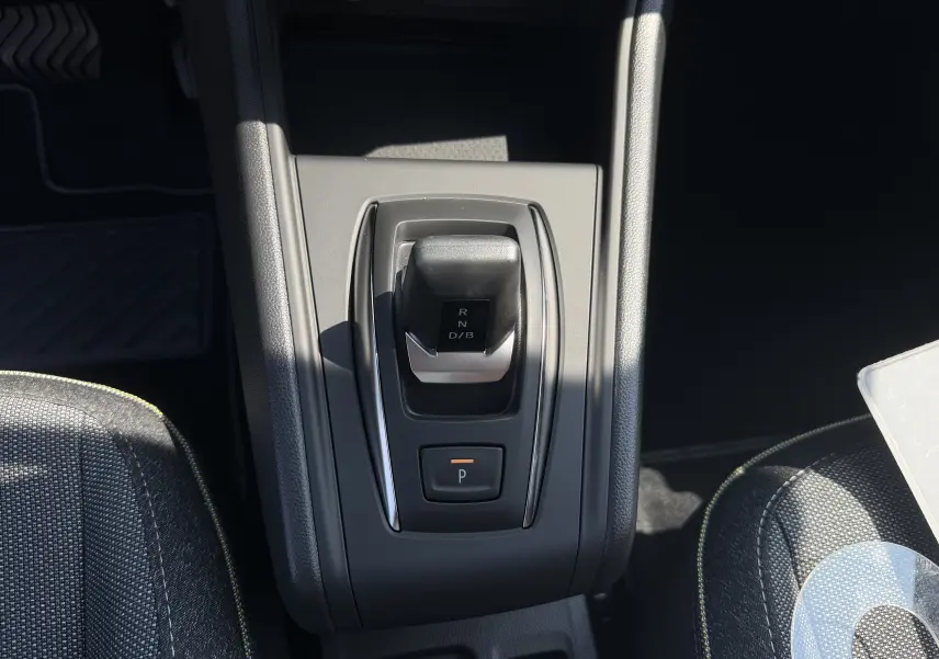 Vue de dessus du levier de vitesses automatique noir sur console centrale grise, entouré de sièges tissu gris avec surpiqûres jaunes.