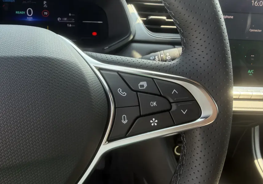 Gros plan sur le volant textile perforé côté droit du Renault Captur 1.8 E-Tech gris Cassiopée, avec commandes multifonctions.