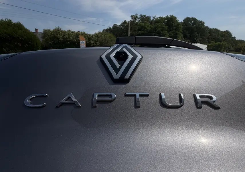 Gros plan sur le logo Renault et l’inscription Captur en chrome sur la peinture gris Cassiopée métallisée du hayon arrière.