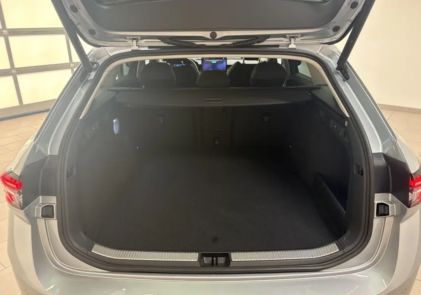 Coffre ouvert vu de l'arrière d'une Skoda Superb Combi gris argent, montrant un espace de chargement spacieux et bien fini.