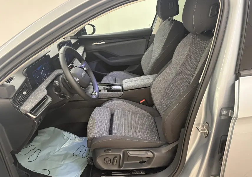 Vue intérieure côté conducteur d'une Skoda Superb Combi gris argent 2025, sièges tissu gris et tableau de bord moderne.
