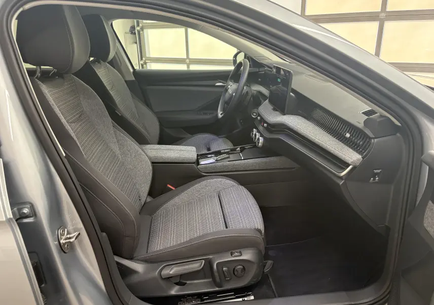 Vue intérieure côté conducteur de la Skoda Superb Combi gris argent, sièges tissu gris et tableau de bord moderne.