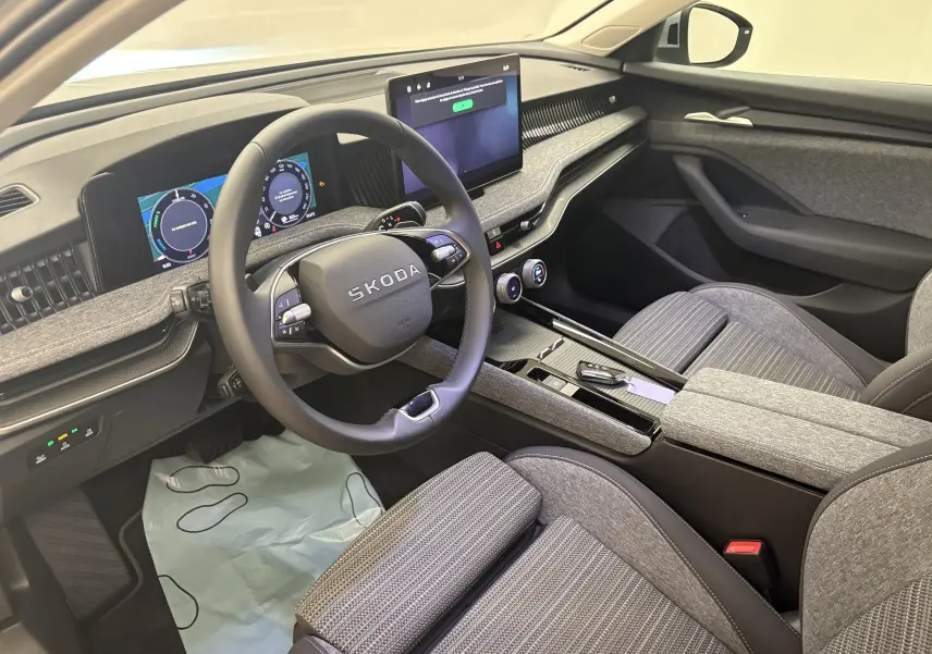 Vue intérieure côté conducteur de la Skoda Superb Combi 2025, tableau de bord gris clair avec écran tactile central et volant multifonction.