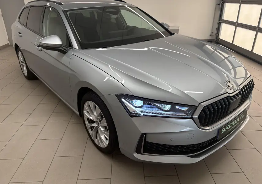 Vue 3/4 avant gauche d'une Skoda Superb Combi gris argent avec phares LED allumés et jantes alliage 18 pouces.