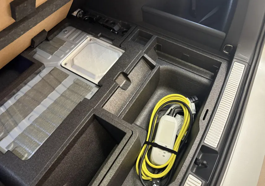 Vue rapprochée du coffre de la Skoda Superb Combi gris argent montrant le rangement avec câble de recharge hybride.