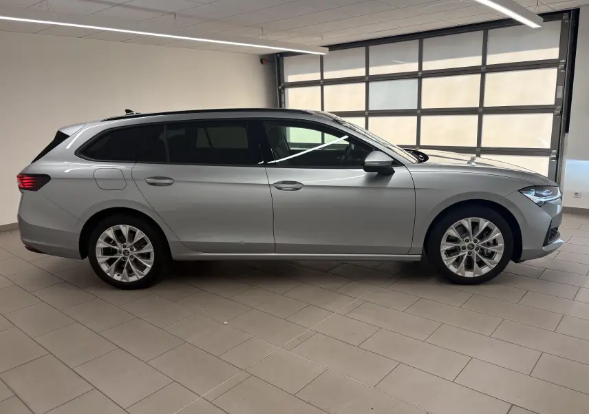 Vue latérale droite d'une Skoda Superb Combi gris argent avec jantes alliage 18 pouces dans un garage lumineux.
