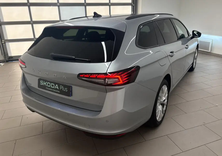 Vue 3/4 arrière droite d'une Skoda Superb Combi gris argent avec feux arrière LED allumés en intérieur showroom.