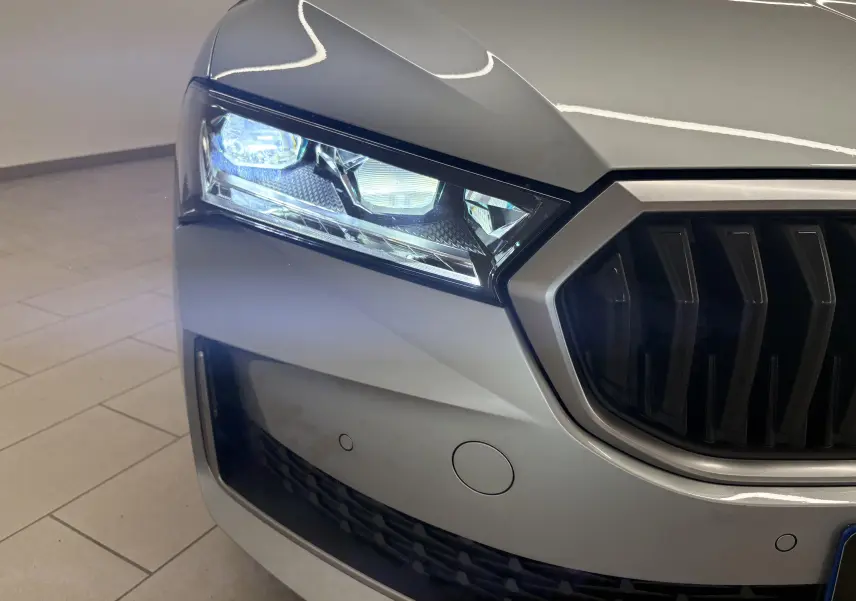 Gros plan sur l'avant gauche gris argent d'une Skoda Superb Combi 2025 avec phare Full Matrix LED allumé et calandre noire.
