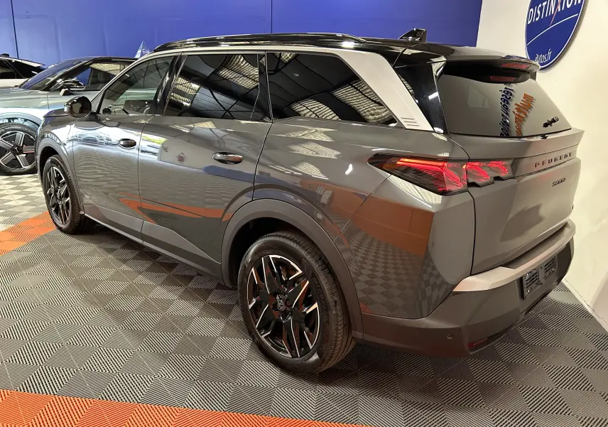 Peugeot 5008 III Hybrid gris titane en 3/4 arrière droit, avec jantes noires et toit noir brillant en showroom.