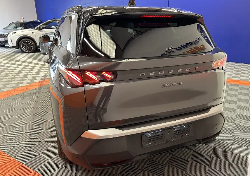 Vue 3/4 arrière droite du Peugeot 5008 gris titane avec feux arrière LED allumés dans un showroom.