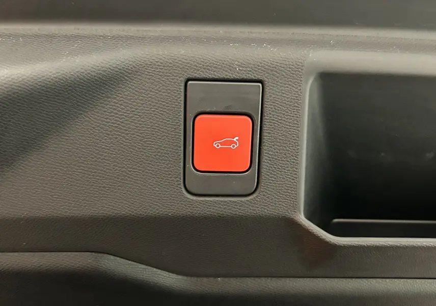 Bouton rouge d'ouverture électrique du coffre sur la garniture intérieure d'un Peugeot 5008 gris titane.