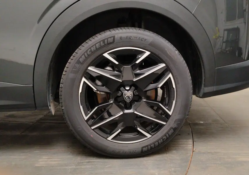 Gros plan sur l’avant droit du Peugeot 5008 gris titane, mettant en valeur le phare LED et la jante noire à inserts métallisés.