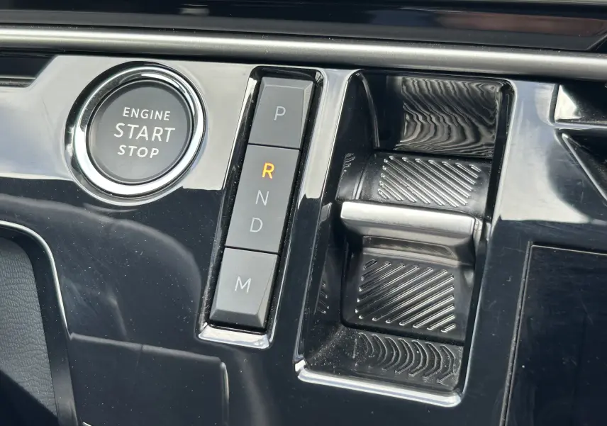 Gros plan sur la console centrale noire brillante du Peugeot 5008 III Hybrid avec bouton start/stop et sélecteur de vitesses automatique.