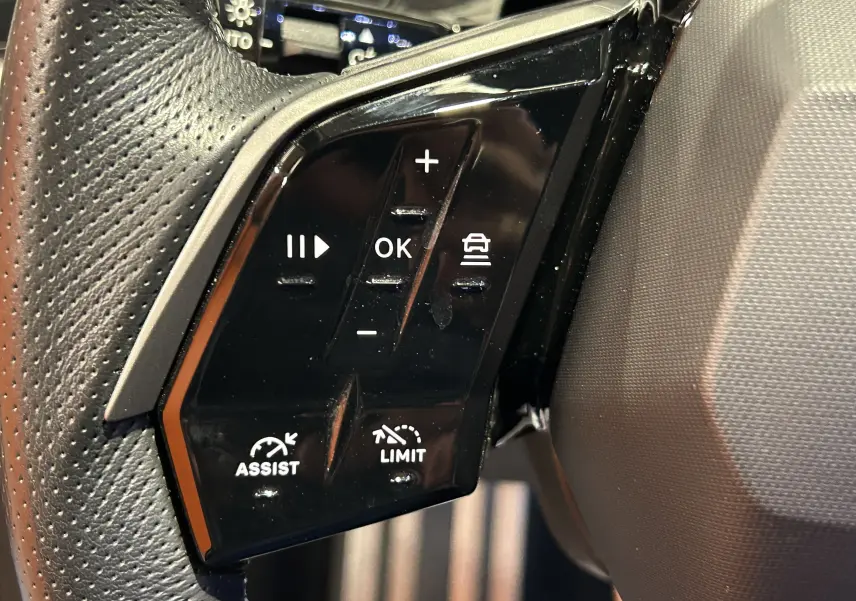Gros plan sur les commandes noires du volant côté gauche du Peugeot 5008 gris Titane, version hybride 2025.