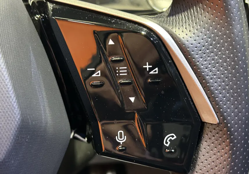 Gros plan sur les commandes noires du volant perforé côté gauche du Peugeot 5008 gris Titane, version hybride 2025.