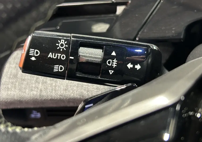 Gros plan sur la commande des feux et clignotants du Peugeot 5008 III Hybrid gris titane, intérieur côté gauche.