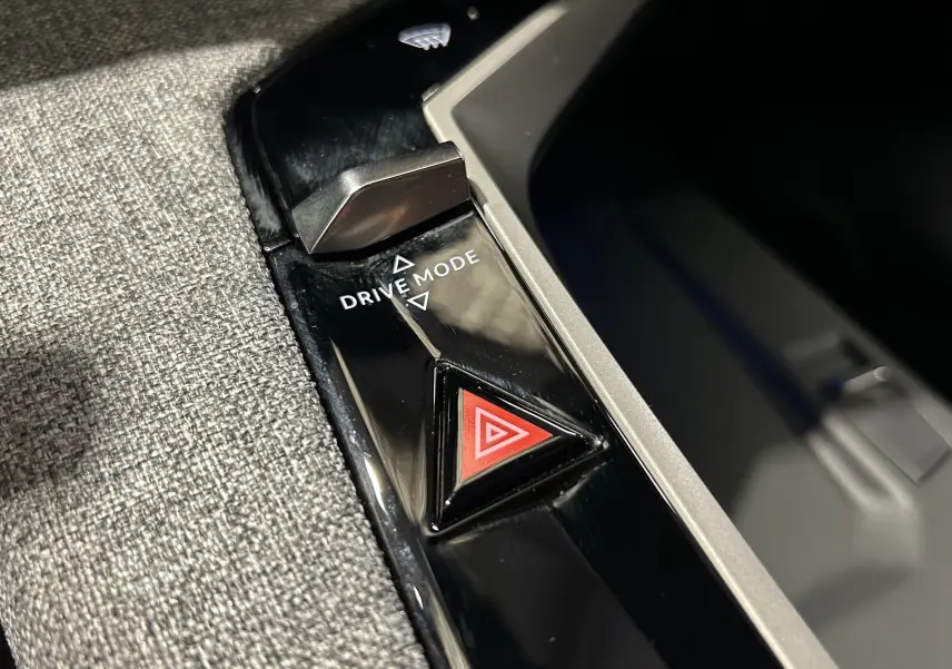 Gros plan sur la console centrale du Peugeot 5008 III Hybrid 145, bouton triangle rouge d’alerte et sélecteur Drive Mode.