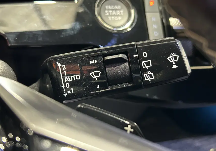 Gros plan sur la commande des essuie-glaces du Peugeot 5008 III Hybrid 145 e-DCS6 GT, avec bouton start visible en arrière-plan.