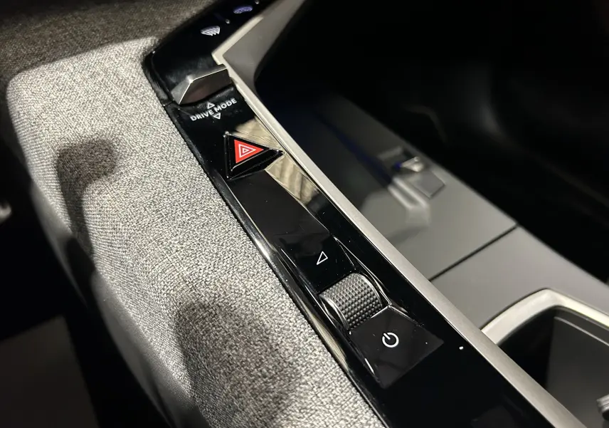 Gros plan sur la console centrale intérieure du Peugeot 5008 III Hybrid 145 GT, tissu gris et commandes noires brillantes.