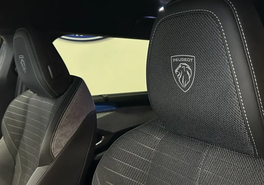 Gros plan sur les sièges avant noirs du Peugeot 5008 III Hybrid 145 GT avec logo lion brodé sur les appuie-têtes.