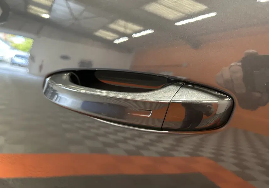 Poignée de porte gris titane métallisée du Peugeot 5008 III Hybrid 145 vue en gros plan avec reflet intérieur.