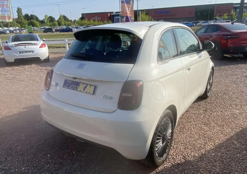 Vue 3/4 arrière droite d'une Fiat 500 électrique blanche avec feux arrière fumés et jantes noires stylisées.