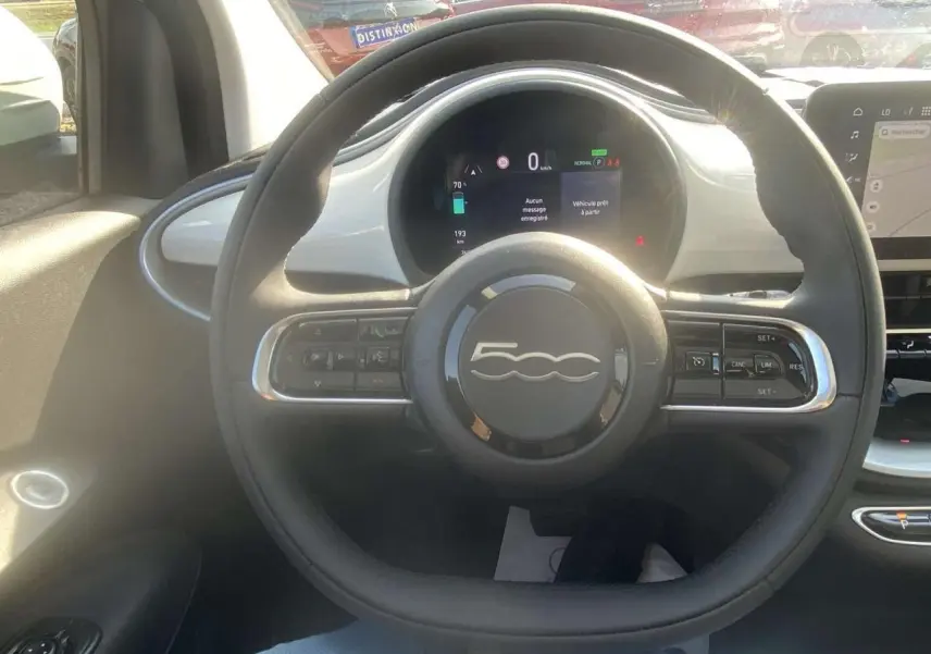 Vue intérieure centrée sur le volant noir de la Fiat 500 électrique blanche avec tableau de bord numérique lumineux.