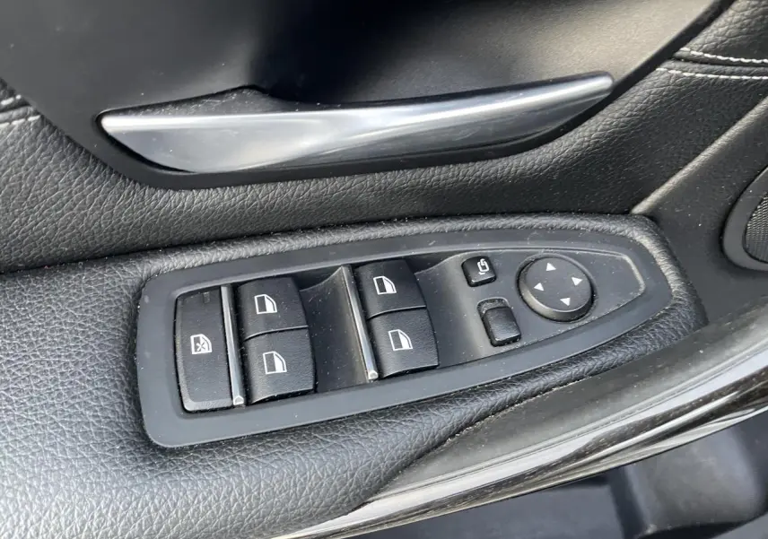 Gros plan sur les commandes de lève-vitres et rétroviseurs côté gauche en cuir noir d'une BMW Série 3 F30 330i xDrive Luxury.