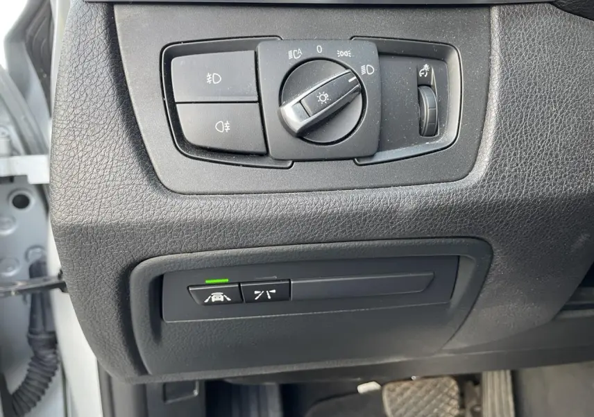 Gros plan sur les commandes d'éclairage et d'assistance au conducteur côté gauche d'une BMW Série 3 F30 gris clair de 2018.