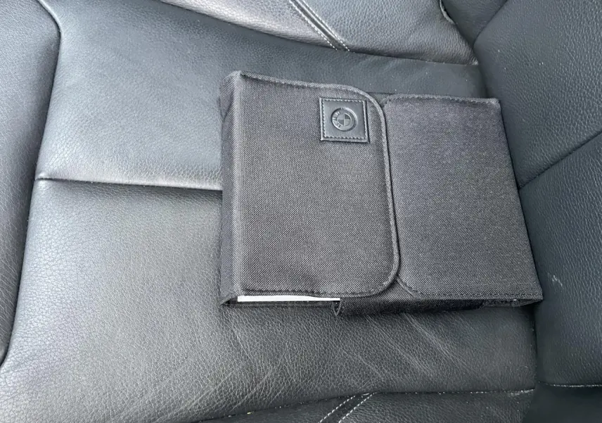 Pochette noire avec logo BMW posée sur la sellerie cuir noire du siège avant d'une BMW Série 3 F30.