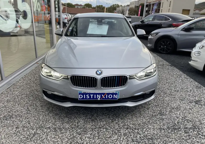 Vue frontale d'une BMW Série 3 F30 gris clair avec calandre chromée et phares LED allumés sur parking.