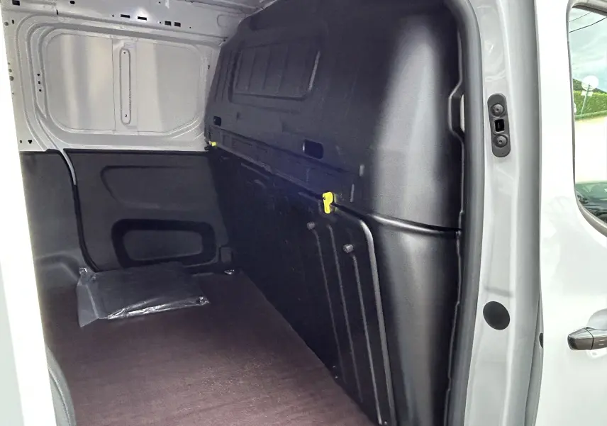 Intérieur du fourgon Peugeot Partner blanc, vue du côté droit montrant le plancher bois et la cloison noire.