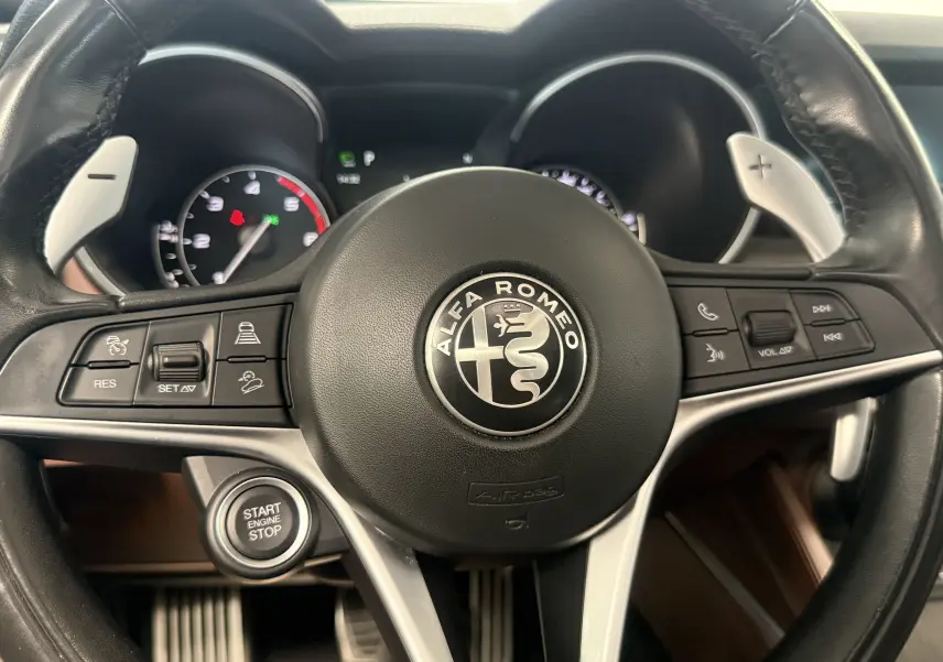 Vue rapprochée du volant cuir noir de l'Alfa Romeo Stelvio 2017 avec commandes intégrées et bouton start engine stop.
