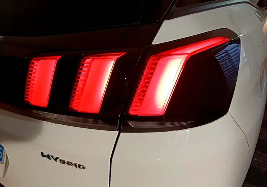 Gros plan sur le feu arrière droit rouge allumé d’un Peugeot 3008 blanc hybride rechargeable, vue arrière.