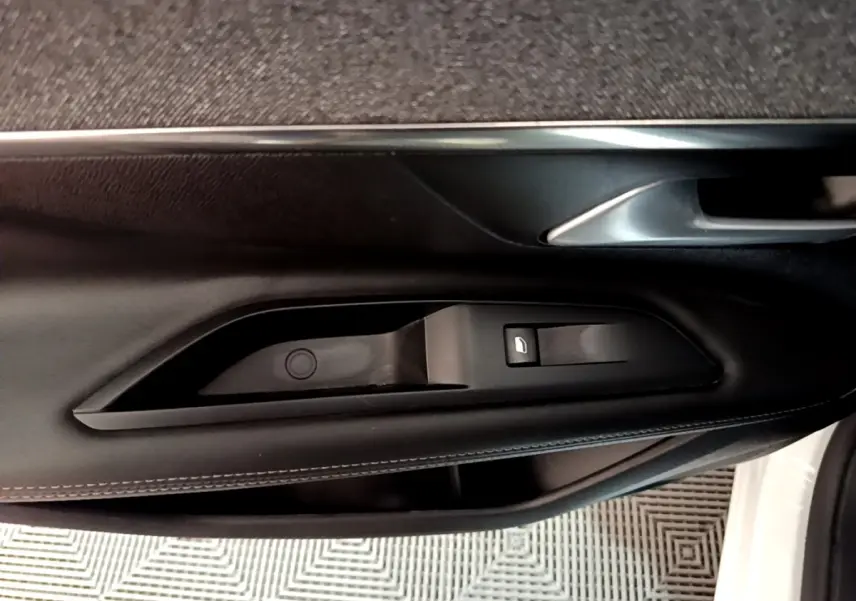 Gros plan sur la commande de lève-vitre côté gauche de la porte intérieure noire du Peugeot 3008 blanc hybride rechargeable.