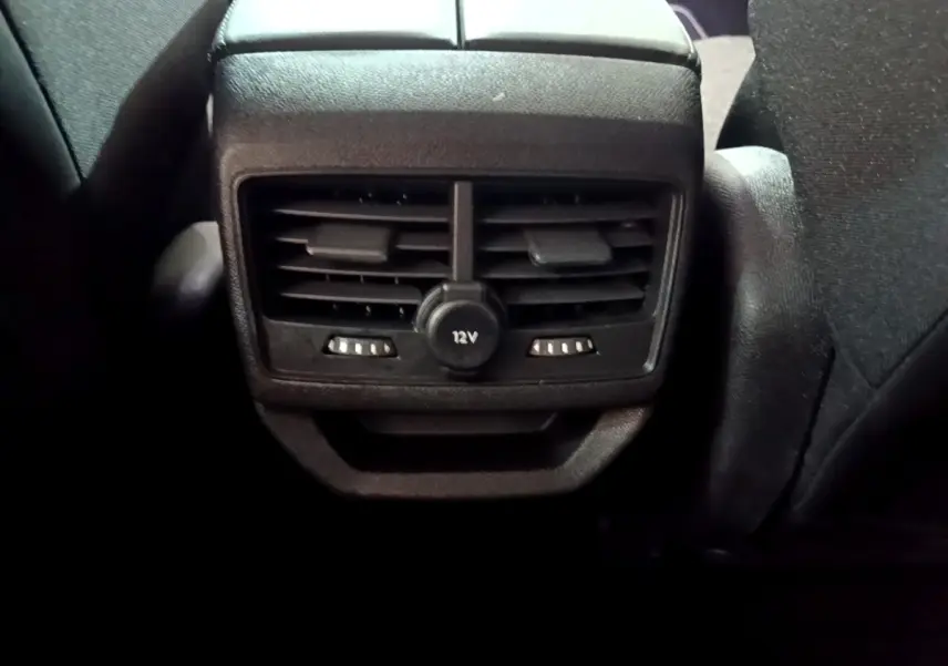 Gros plan sur la sortie d’air arrière noire avec prise 12V du Peugeot 3008 hybride rechargeable blanc, intérieur sombre.