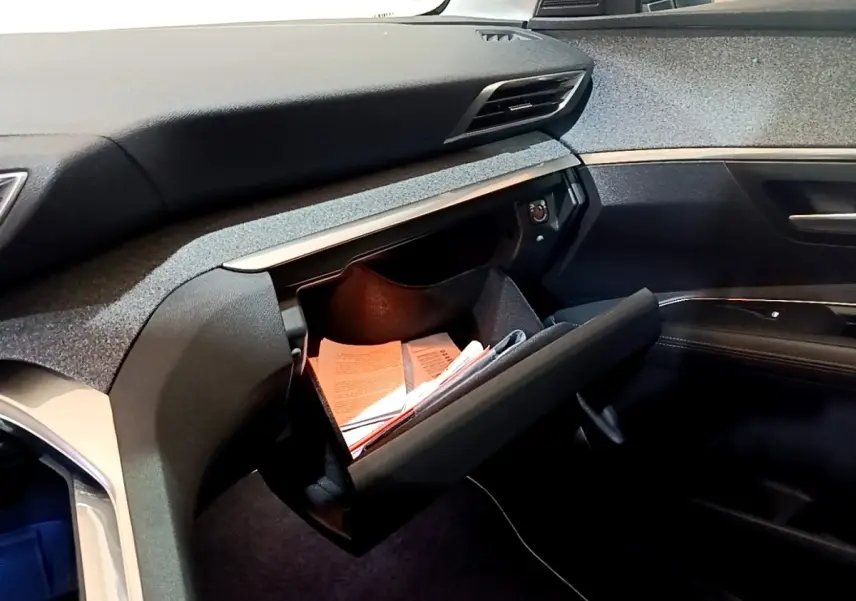 Intérieur côté passager du Peugeot 3008 hybride blanc, boîte à gants ouverte avec documents visibles, tableau de bord moderne.