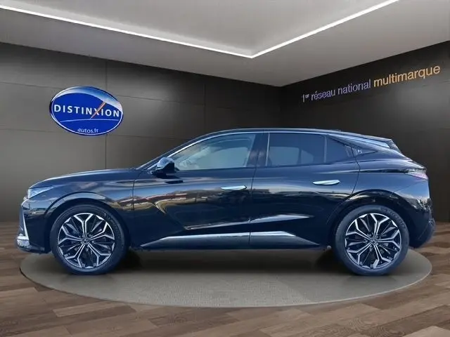 Vue latérale droite d'une DS4 noire 2022 avec jantes alliage distinctives et spoiler de coffre visible en intérieur showroom.