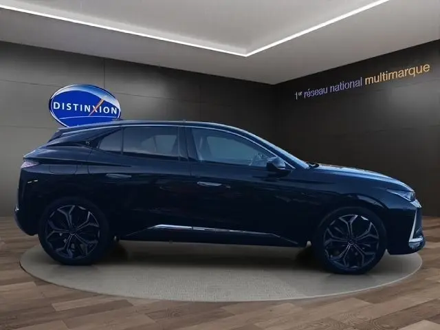 Profil droit de la DS4 BlueHDi 130 Rivoli 2022 noire, avec jantes noires et spoiler de coffre visible en showroom.