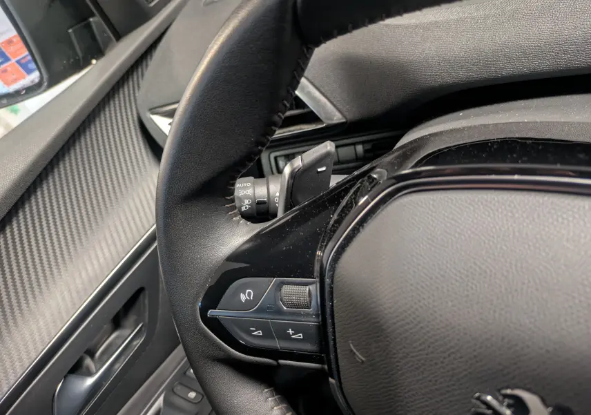 Gros plan sur le volant cuir noir du Peugeot 5008 2024, avec commandes intégrées et tableau de bord partiel visible.