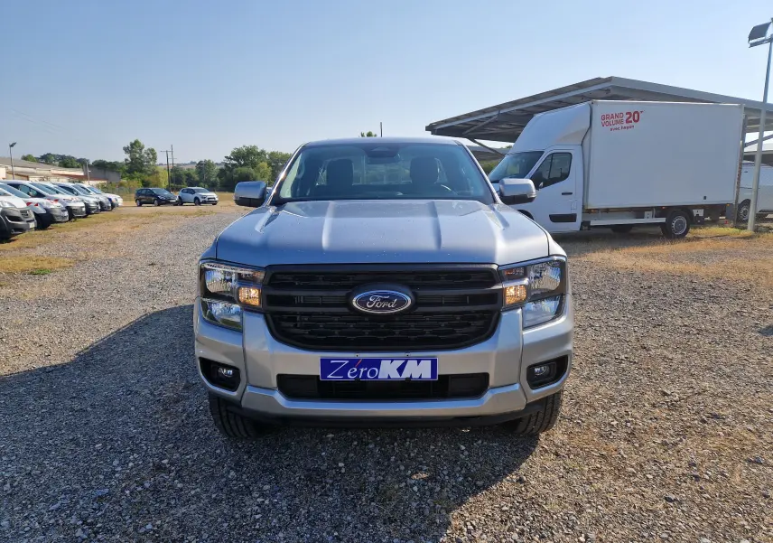Vue avant frontale du Ford Ranger Super Cabine gris Iconic, avec calandre noire et phares allumés sur terrain gravillonné.