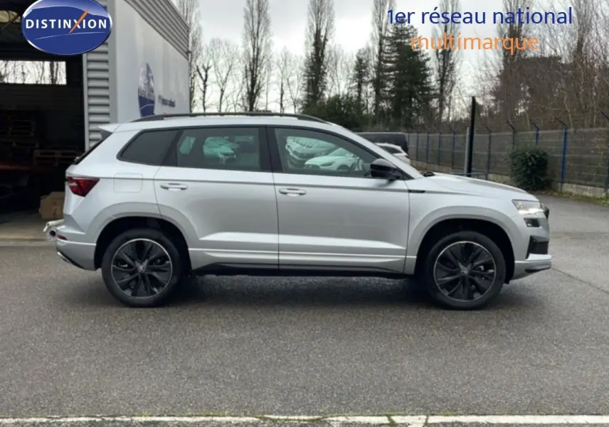 Vue de profil côté gauche d’un Skoda Karoq gris argent métallisé 2025 avec jantes noires et toit panoramique.